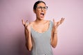 Young beautiful woman wearing casual striped dress and glasses over pink background crazy and mad shouting and yelling with Royalty Free Stock Photo