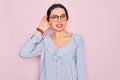 Young beautiful woman wearing casual striped shirt and glasses over pink background smiling with hand over ear listening an Royalty Free Stock Photo