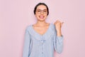 Young beautiful woman wearing casual striped shirt and glasses over pink background smiling with happy face looking and pointing Royalty Free Stock Photo