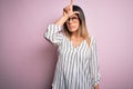 Young beautiful woman wearing casual striped t-shirt and glasses over pink background making fun of people with fingers on Royalty Free Stock Photo