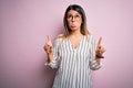 Young beautiful woman wearing casual striped t-shirt and glasses over pink background Pointing up looking sad and upset, Royalty Free Stock Photo