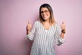 Young beautiful woman wearing casual striped t-shirt and glasses over pink background success sign doing positive gesture with Royalty Free Stock Photo