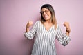 Young beautiful woman wearing casual striped t-shirt and glasses over pink background very happy and excited doing winner gesture Royalty Free Stock Photo