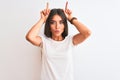 Young beautiful woman wearing casual t-shirt standing over isolated white background doing funny gesture with finger over head as Royalty Free Stock Photo