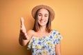 Young beautiful woman wearing casual t-shirt and summer hat over isolated yellow background smiling friendly offering handshake as Royalty Free Stock Photo