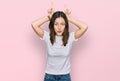 Young beautiful woman wearing casual white t shirt doing funny gesture with finger over head as bull horns Royalty Free Stock Photo