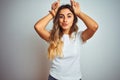 Young beautiful woman wearing casual white t-shirt over isolated background doing funny gesture with finger over head as bull Royalty Free Stock Photo