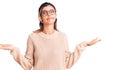 Young beautiful woman wearing casual winter sweater and glasses clueless and confused expression with arms and hands raised Royalty Free Stock Photo