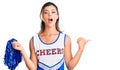 Young beautiful woman wearing cheerleader uniform surprised pointing with hand finger to the side, open mouth amazed expression Royalty Free Stock Photo