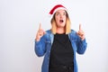 Young beautiful woman wearing Christmas Santa hat standing over isolated white background amazed and surprised looking up and Royalty Free Stock Photo