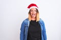 Young beautiful woman wearing Christmas Santa hat standing over isolated white background sticking tongue out happy with funny Royalty Free Stock Photo