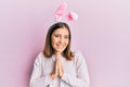 Young beautiful woman wearing cute easter bunny ears praying with hands together asking for forgiveness smiling confident