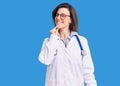 Young beautiful woman wearing doctor stethoscope and glasses looking confident at the camera with smile with crossed arms and hand Royalty Free Stock Photo