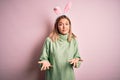 Young beautiful woman wearing easter rabbit ears standing over isolated pink background clueless and confused expression with arms