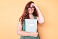 Young beautiful woman wearing glasses holding book stressed and frustrated with hand on head, surprised and angry face Royalty Free Stock Photo