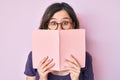 Young beautiful woman wearing glasses reading book afraid and shocked with surprise and amazed expression, fear and excited face Royalty Free Stock Photo