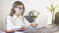A young beautiful woman wearing glasses typing at her laptop in office. Medium shot Royalty Free Stock Photo