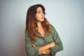 Young beautiful woman wearing green shirt standing over grey isolated background looking to the side with arms crossed convinced Royalty Free Stock Photo