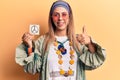 Young beautiful woman wearing hippie clothes holding peace reminder smiling happy and positive, thumb up doing excellent and Royalty Free Stock Photo