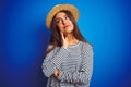 Young beautiful woman wearing navy striped t-shirt and hat over isolated blue background with hand on chin thinking about Royalty Free Stock Photo