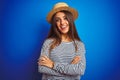 Young beautiful woman wearing navy striped t-shirt and hat over isolated blue background happy face smiling with crossed arms Royalty Free Stock Photo