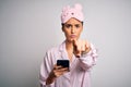 Young beautiful woman wearing pajama and sleep mask having conversation using smartphone pointing with finger to the camera and to Royalty Free Stock Photo