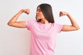 Young beautiful woman wearing pink casual t-shirt standing over isolated white background showing arms muscles smiling proud Royalty Free Stock Photo