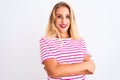 Young beautiful woman wearing pink striped t-shirt standing over isolated white background happy face smiling with crossed arms Royalty Free Stock Photo