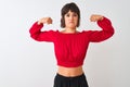 Young beautiful woman wearing red summer t-shirt standing over isolated white background showing arms muscles smiling proud Royalty Free Stock Photo