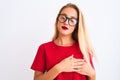 Young beautiful woman wearing red t-shirt and glasses standing over isolated white background smiling with hands on chest with Royalty Free Stock Photo