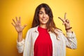 Young beautiful woman wearing red t-shirt and stripes shirt over yellow isolated background showing and pointing up with fingers