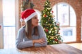 Young beautiful woman wearing santa claus hat at the table at home around christmas decoration looking to side, relax profile pose Royalty Free Stock Photo