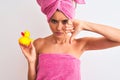 Young beautiful woman wearing shower towel holding duck over isolated white background with angry face, negative sign showing