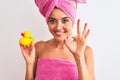 Young beautiful woman wearing shower towel holding duck over isolated white background doing ok sign with fingers, excellent Royalty Free Stock Photo