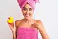 Young beautiful woman wearing shower towel holding duck over isolated white background with surprise face pointing finger to Royalty Free Stock Photo