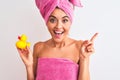 Young beautiful woman wearing shower towel holding duck over isolated white background very happy pointing with hand and finger to Royalty Free Stock Photo