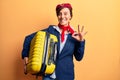 Young beautiful woman wearing stewardess uniform holding cabin bag doing ok sign with fingers, smiling friendly gesturing