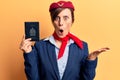 Young beautiful woman wearing stewardess uniform holding canadian passport scared and amazed with open mouth for surprise,