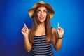 Young beautiful woman wearing striped t-shirt and summer hat over isolated blue background amazed and surprised looking up and Royalty Free Stock Photo