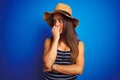 Young beautiful woman wearing striped t-shirt and summer hat over isolated blue background looking stressed and nervous with hands Royalty Free Stock Photo