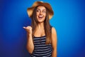 Young beautiful woman wearing striped t-shirt and summer hat over isolated blue background smiling with happy face looking and Royalty Free Stock Photo