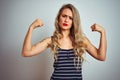 Young beautiful woman wearing stripes t-shirt standing over white isolated background showing arms muscles smiling proud Royalty Free Stock Photo