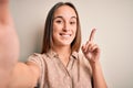 Young beautiful woman wearing summer shirt making selfie by camera over white background surprised with an idea or question Royalty Free Stock Photo