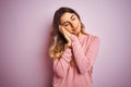 Young beautiful woman wearing a sweater over pink  background sleeping tired dreaming and posing with hands together while Royalty Free Stock Photo