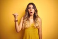 Young beautiful woman wearing t-shirt over yellow isolated background Surprised pointing with hand finger to the side, open mouth Royalty Free Stock Photo
