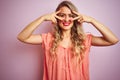 Young beautiful woman wearing t-shirt standing over pink isolated background Doing peace symbol with fingers over face, smiling Royalty Free Stock Photo