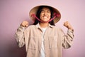 Young beautiful woman wearing traditional conical asian hat over isolated pink background very happy and excited doing winner Royalty Free Stock Photo