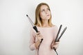 Young beautiful woman wearing trendy pink dress holding curling iron and hair streightener on isolated white background Royalty Free Stock Photo