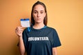 Young beautiful woman wearing volunteer t-shirt doing volunteering holding id pass card with a confident expression on smart face