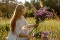 Young beautiful woman, wearing white dress, holding flowers on the meadow. Girl joying nature and freedom. Natural